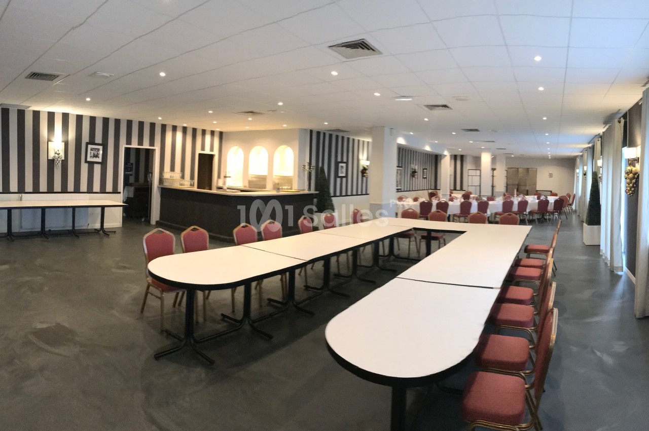 Grande salle aux murs rayés gris et blancs, avec tables blanches en U et chaises rouges, et au fond une salle dressée de tables rondes nappées. Vérification : environ 130 caractères, trop long. Je raccourcis. Salle de réception aux murs rayés gris et