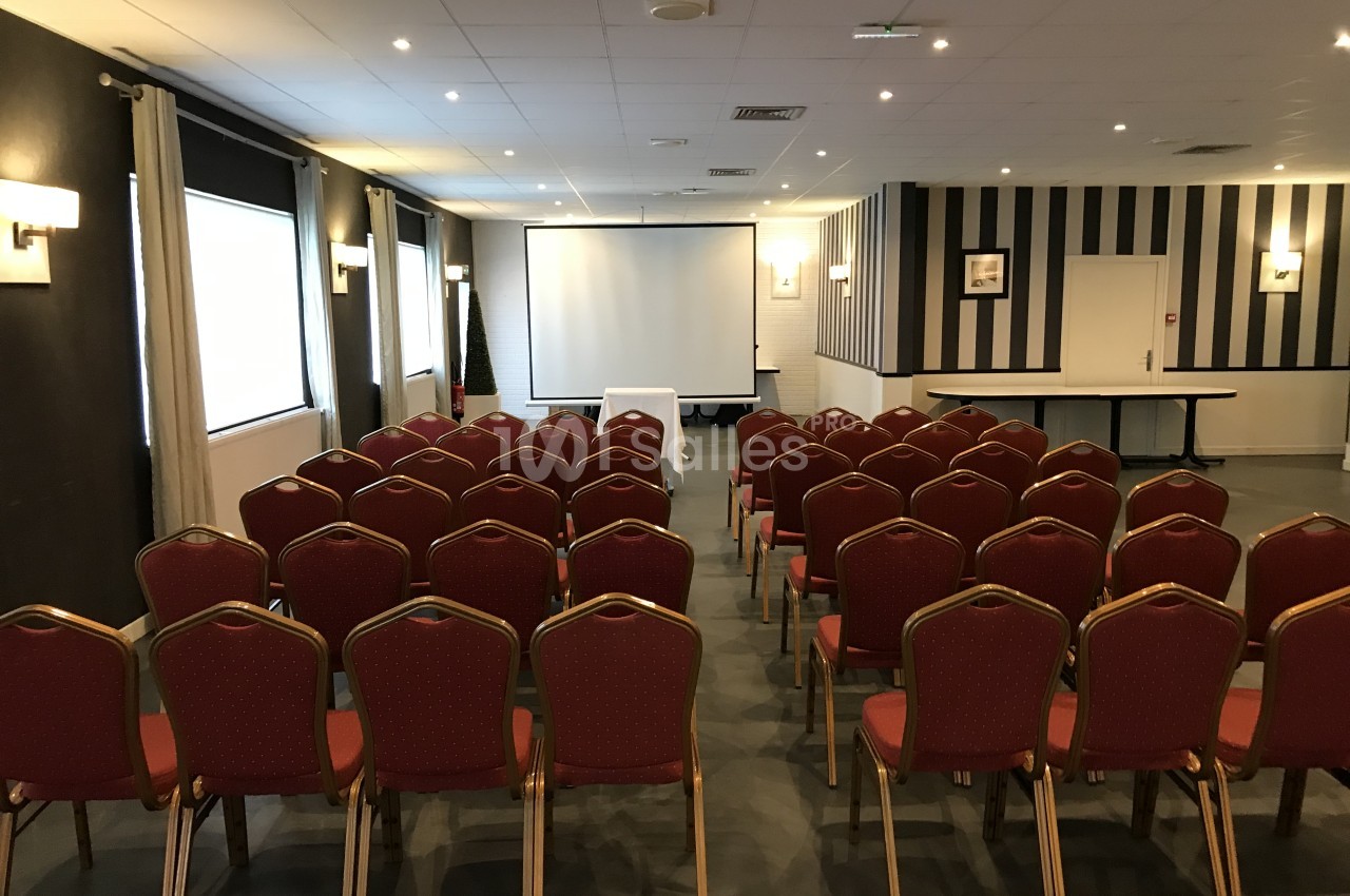 Salle de réunion en mode conférence avec rangées de chaises rouges face à un écran de projection, murs rayés noir et blanc, éclairage au plafond. Let me check length: roughly 150 characters, too long. Need ≤125. Salle de conférence aménagée en rangs de