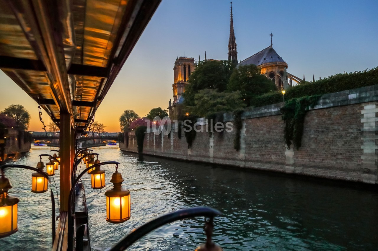 Lanternes allumées sur le pont d'une péniche au crépuscule, face à la cathédrale Notre-Dame le long de la Seine.