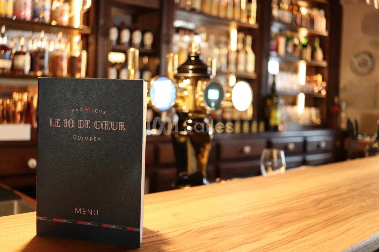 Un menu noir posé sur un comptoir en bois, devant des étagères garnies de bouteilles et une pompe à bière dorée.