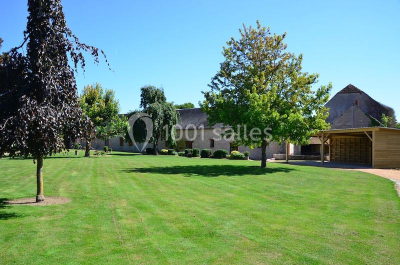 Vue d'un grand jardin avec pelouse bien entretenue, arbres et bâtiments en pierre sous un ciel bleu.