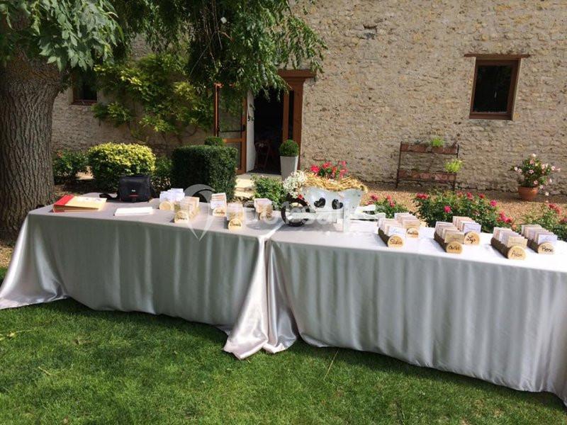 Tables recouvertes de nappes blanches disposées sur une pelouse, ornées de cartons et décorations, devant un bâtiment en…