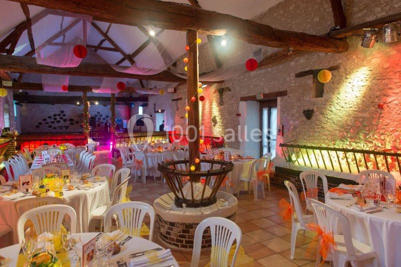 Salle de réception décorée avec des tables rondes, des chaises blanches et des guirlandes lumineuses suspendues.