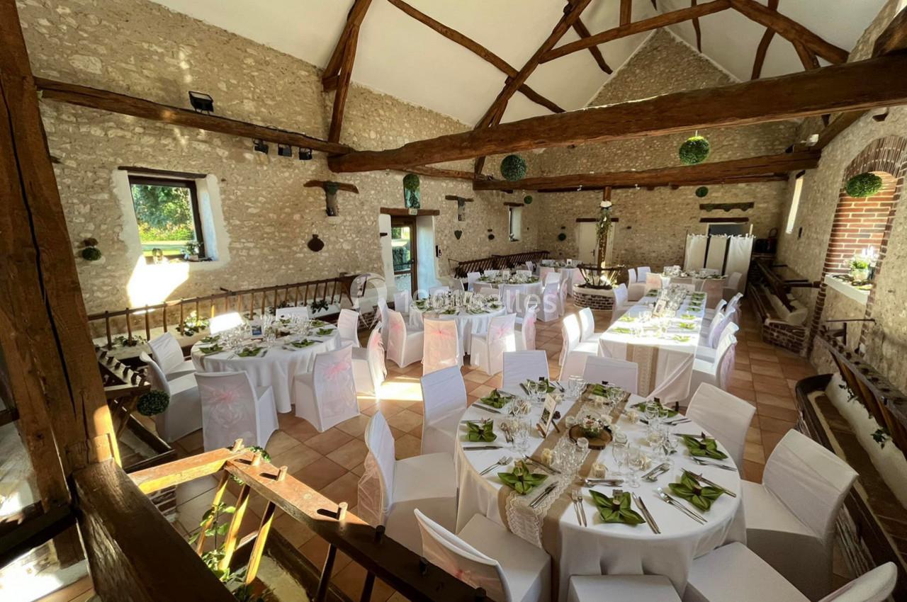 Salle de réception rustique avec murs en pierre, poutres apparentes et tables élégamment dressées pour un événement.