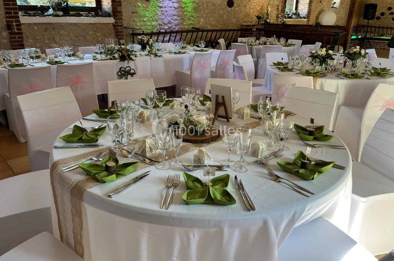 Tables rondes élégamment dressées pour un événement, avec nappes blanches, serviettes vertes et décorations florales.