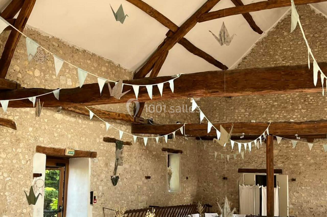 Salle en pierre avec poutres apparentes, décorée de guirlandes et origamis suspendus pour un événement.