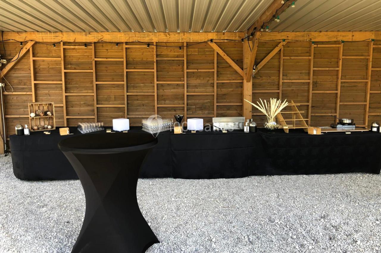 Table de buffet noir sous un abri en bois, avec divers plats, décorations et une table haute en premier plan.
