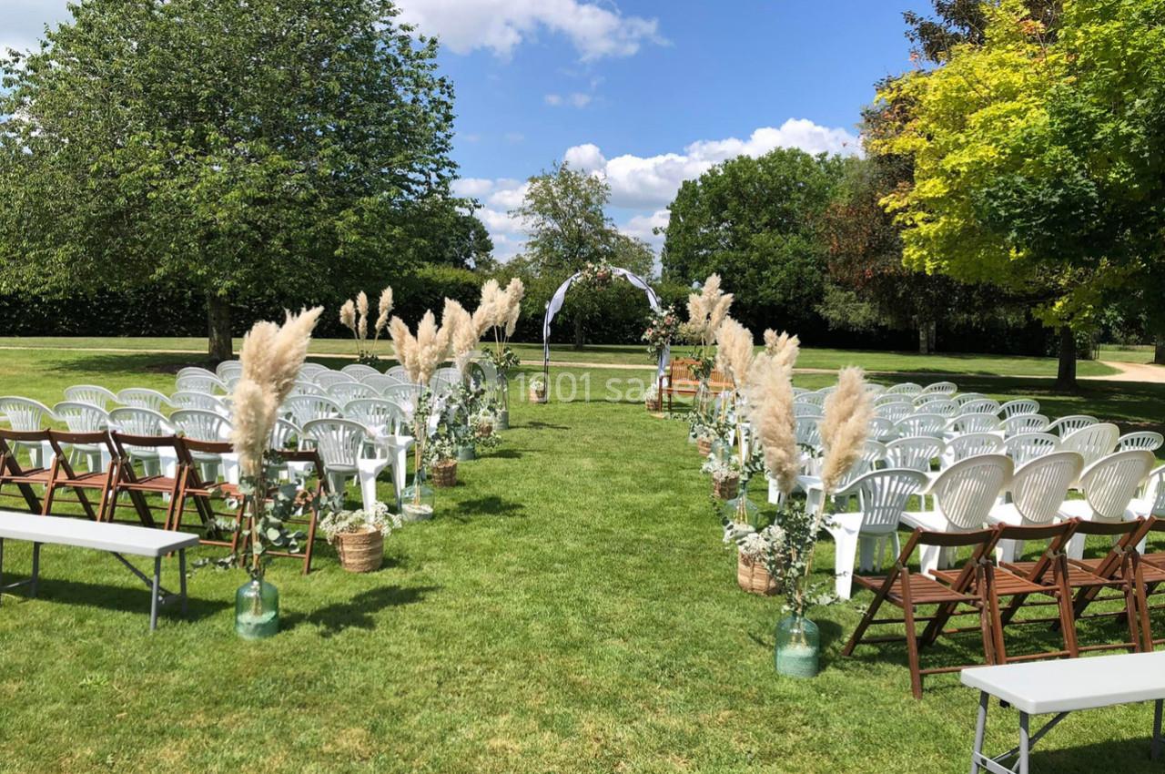 Chaises blanches et marron disposées en rangées dans un jardin, décorées de plantes et de pampas pour une cérémonie en plein…