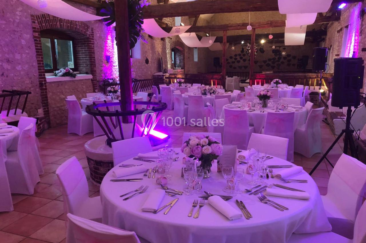 Salle de réception décorée avec des tables rondes dressées, éclairage violet et ambiance chaleureuse.