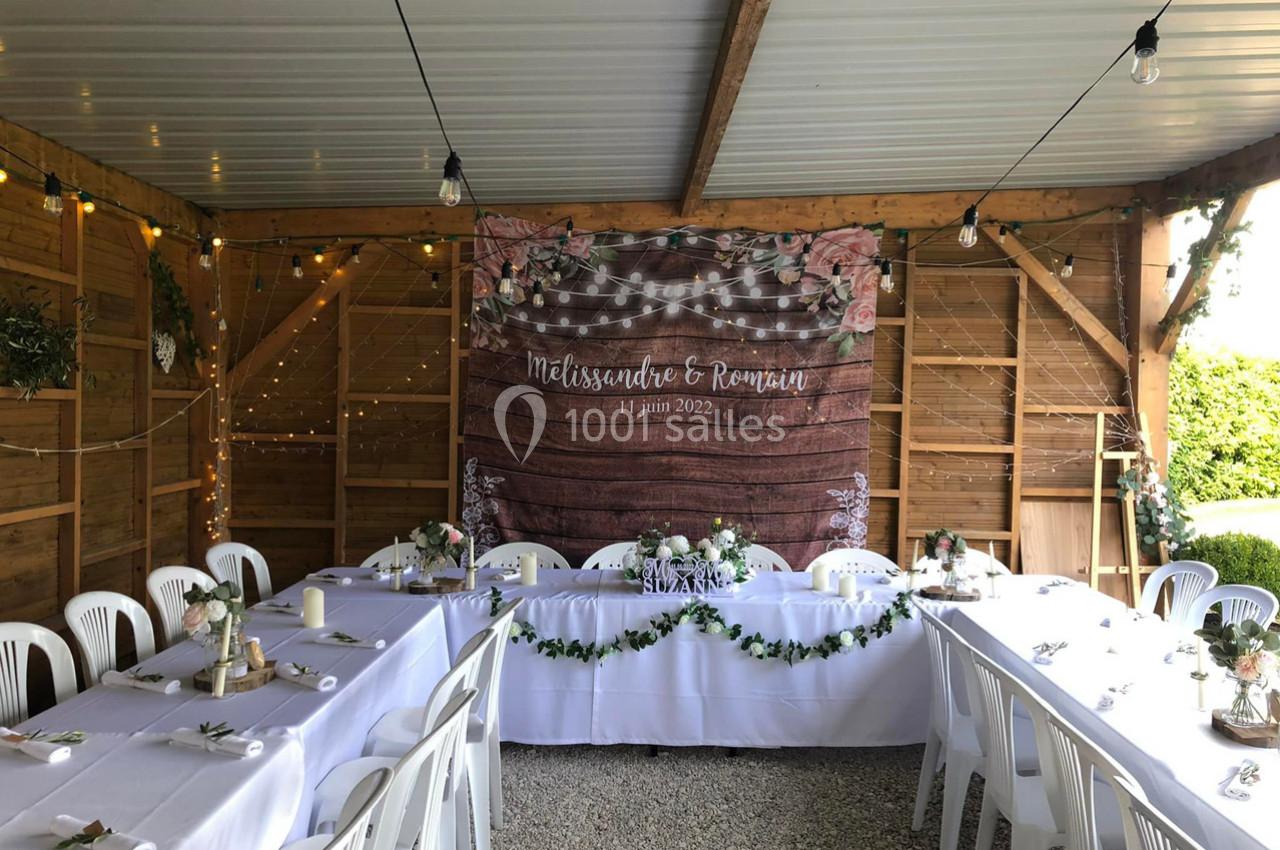 Salle décorée pour un mariage avec tables blanches, guirlandes lumineuses et une bannière personnalisée en fond.