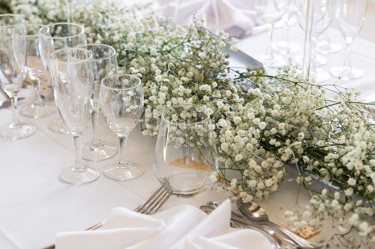 Table dressée avec nappes blanches, verres, couverts et décoration florale de gypsophile blanche.