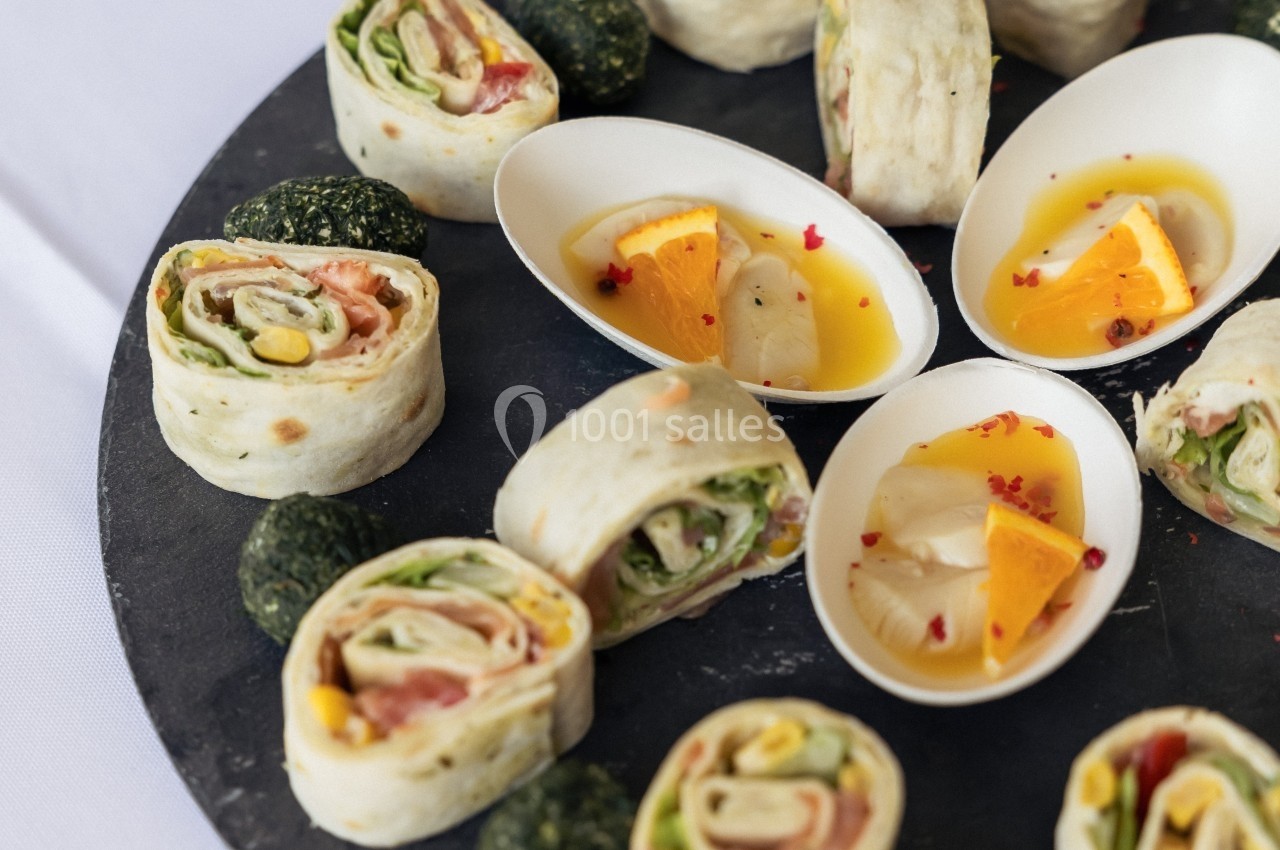 Plateau de wraps garnis et de petites verrines avec des morceaux de fromage et d'orange, présenté sur une table.