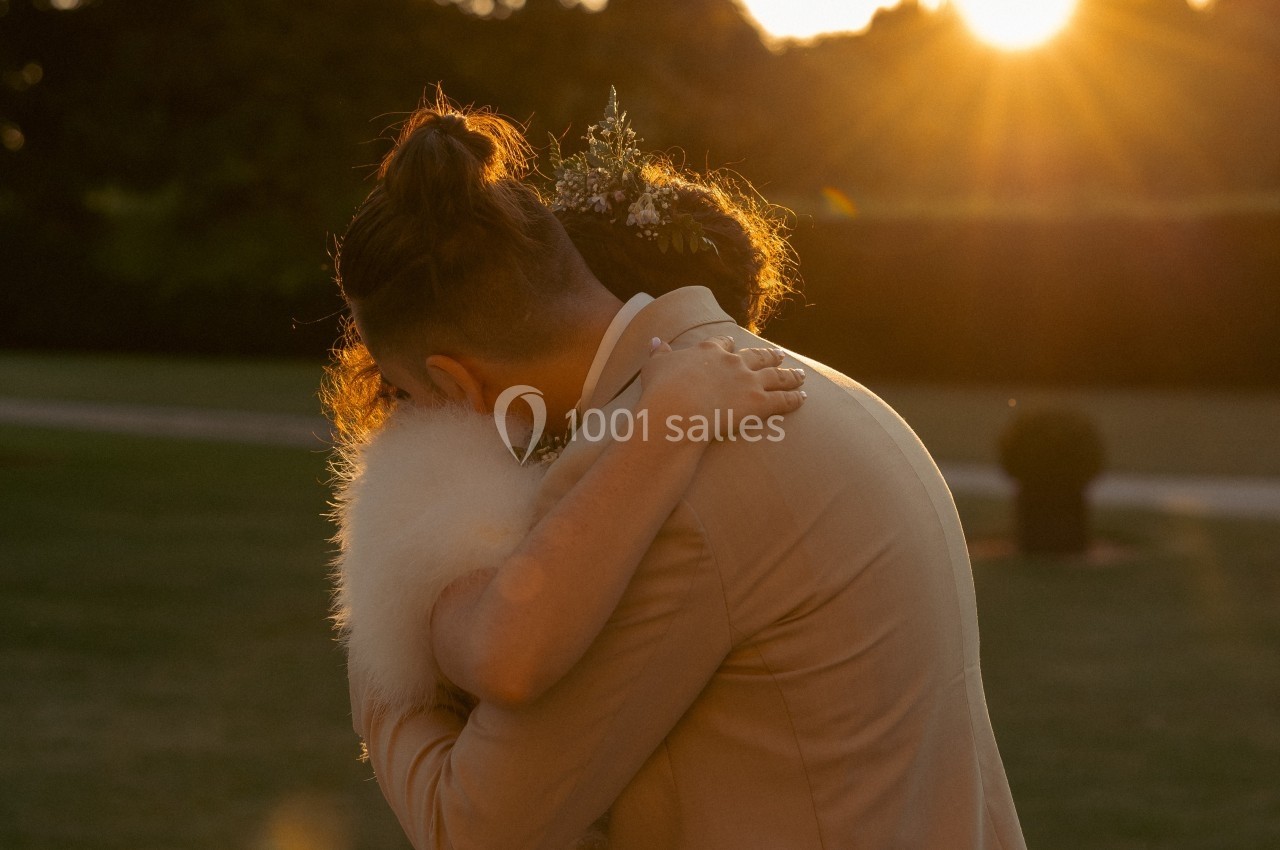 Un couple s'enlace tendrement dans un parc au coucher du soleil, entouré de verdure.