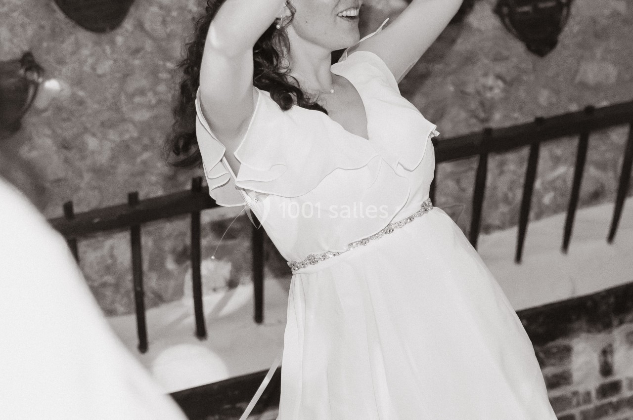 Femme en robe légère et lunettes en forme de cœur dansant joyeusement devant un mur en pierre.