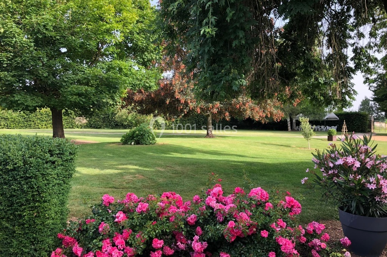 Massif de fleurs roses au premier plan, pelouse verdoyante et arbres ombragés en arrière-plan d'un jardin paisible.