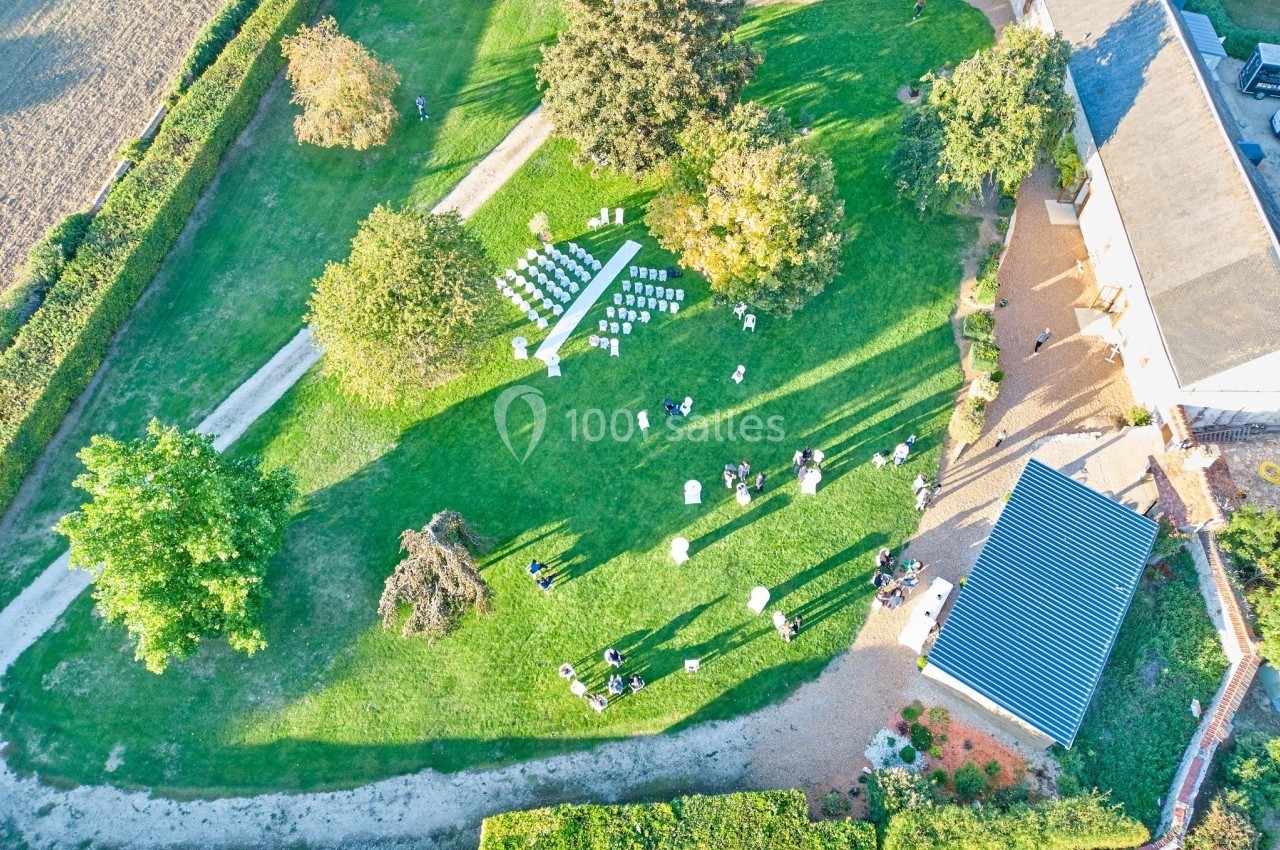 Vue aérienne d'un jardin avec des chaises disposées pour un événement et des personnes rassemblées à différents endroits.