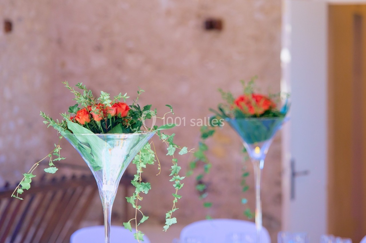 Deux vases en verre transparent garnis de fleurs rouges et de feuillage, posés sur une table dans un décor lumineux.