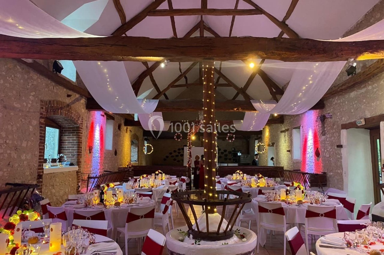 Salle de réception décorée avec des tables dressées, des guirlandes lumineuses et des voilages suspendus au plafond.