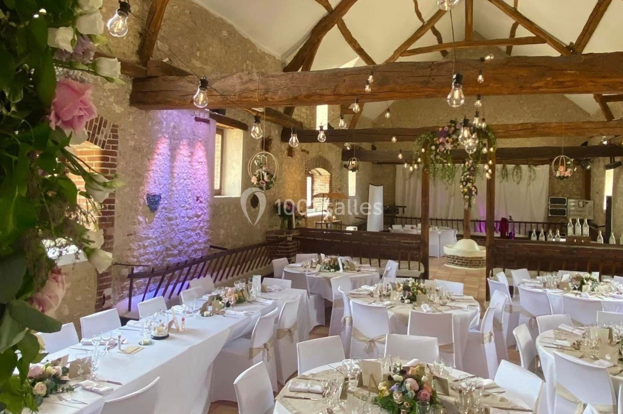 Salle de réception décorée avec des tables dressées, des fleurs et des guirlandes lumineuses suspendues au plafond.
