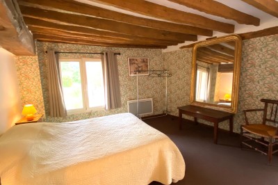 Chambre lumineuse avec poutres apparentes, lit double, miroir doré, chaise en bois et vue sur une fenêtre.