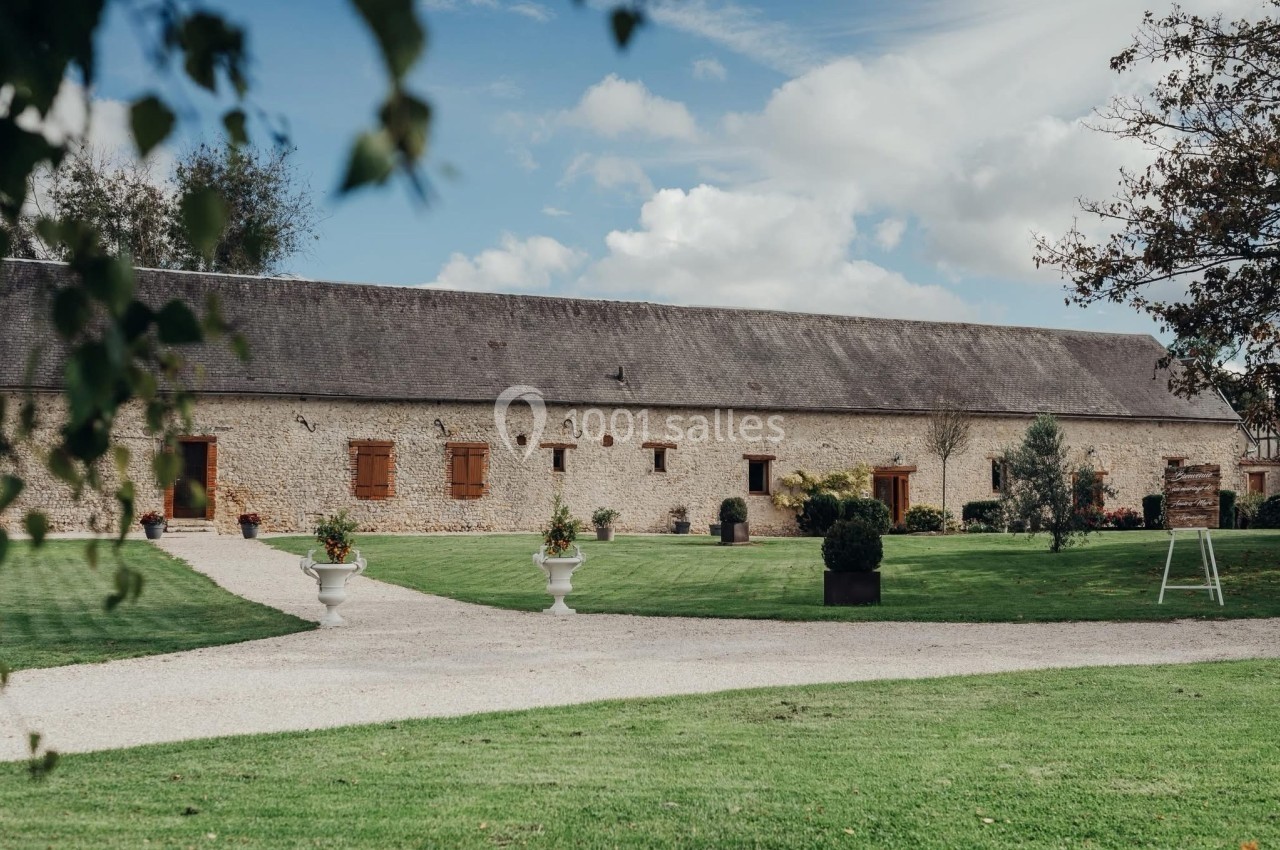 Bâtiment en pierre avec toit en ardoise, entouré d'une pelouse bien entretenue et d'un chemin gravillonné.