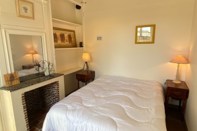 Chambre lumineuse avec poutres apparentes, lit double, miroir doré, chaise en bois et vue sur une fenêtre.
