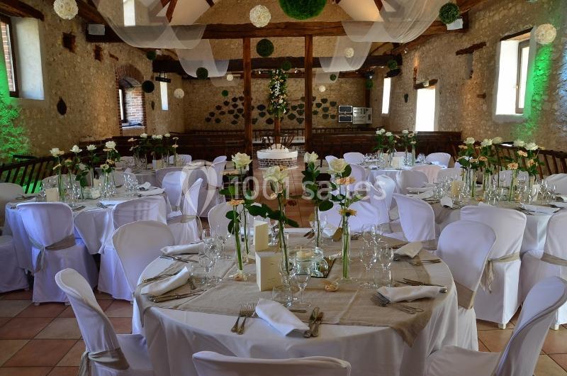 Salle de réception décorée avec des tables rondes, nappes blanches, chaises houssées et centres de table fleuris.
