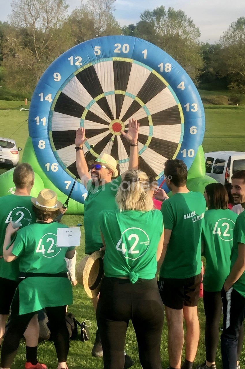 Un groupe de personnes en t-shirts verts participe à une activité de fléchettes géantes en plein air.
