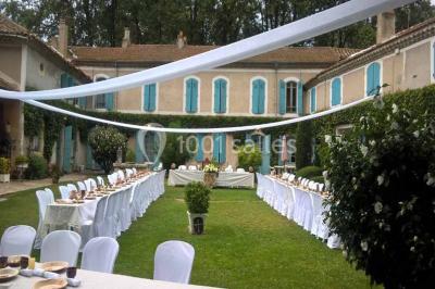Un homme en costume soulève une femme en robe blanche dans un jardin au coucher du soleil.