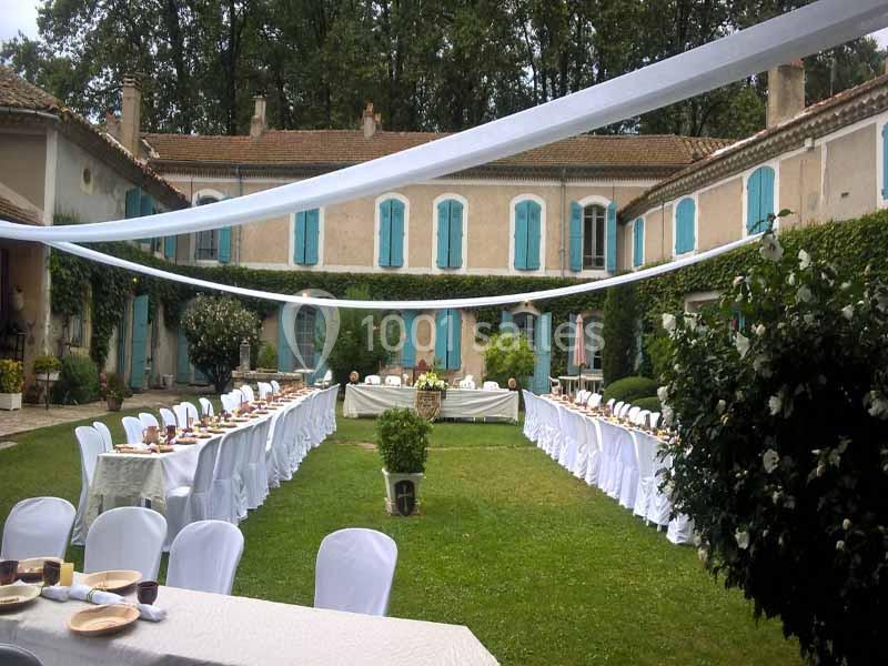 Cour d'une maison ancienne avec tables dressées en extérieur, chaises blanches et décorations pour un événement.
