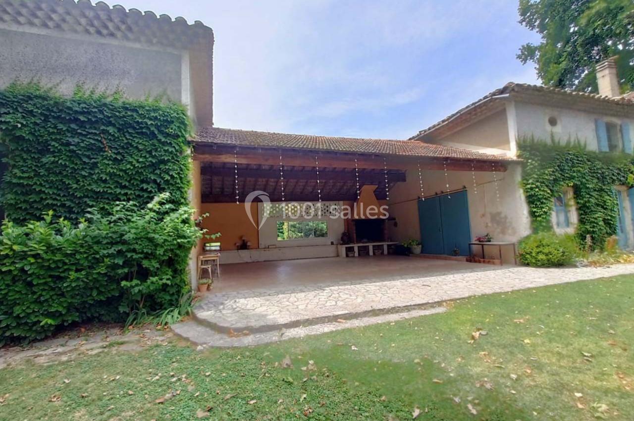 Grande terrasse couverte avec cheminée, entourée de murs et de végétation, dans un cadre extérieur verdoyant.