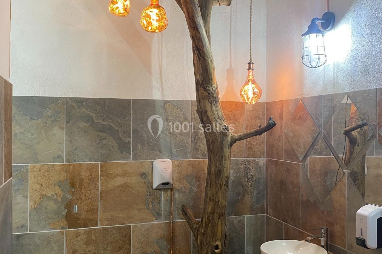 Salle de bain rustique avec lavabo double, éclairage suspendu et décoration en bois brut intégrée.