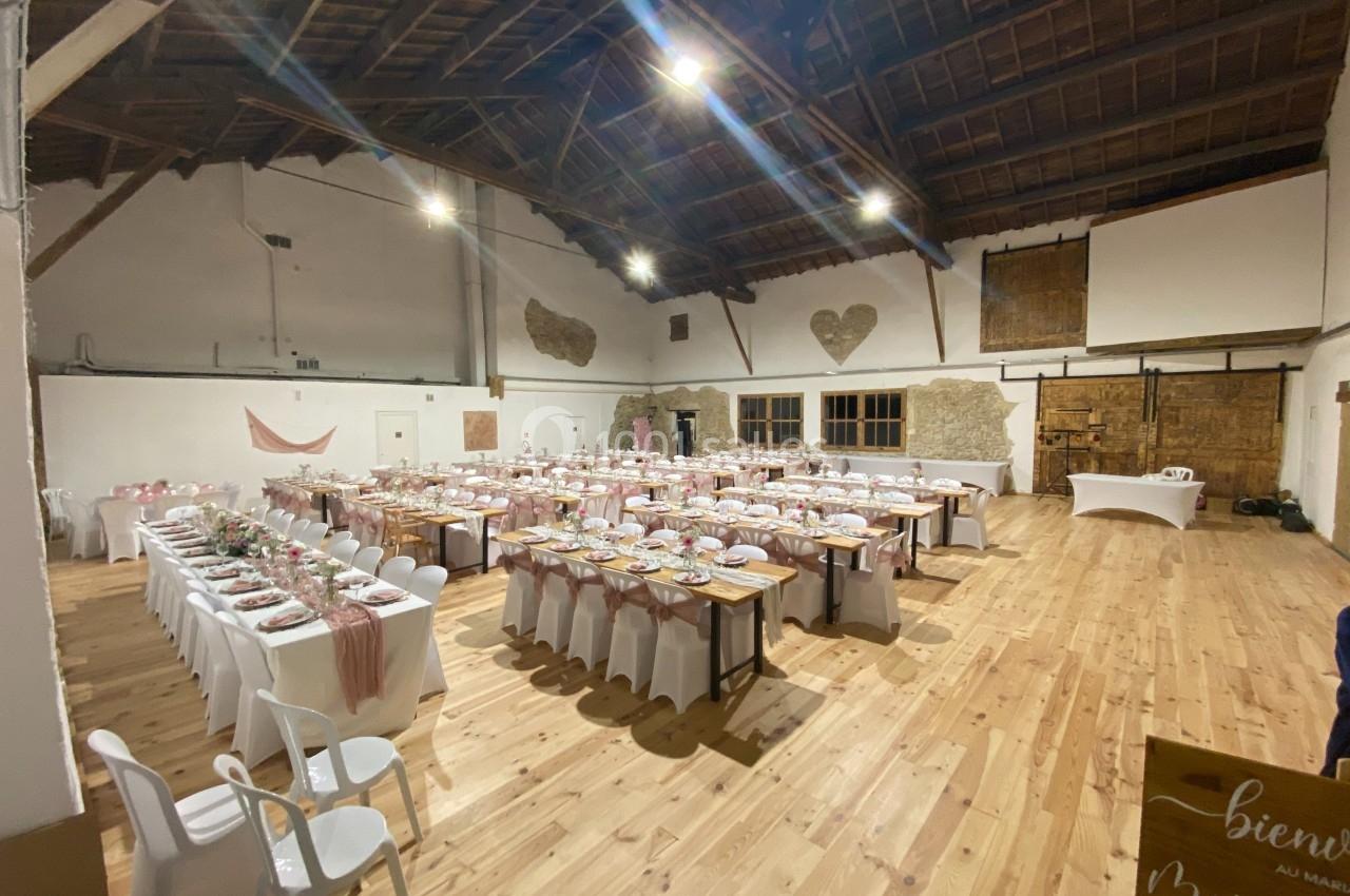 Salle de réception décorée pour un mariage, avec de longues tables dressées et des chaises blanches dans un espace en bois.