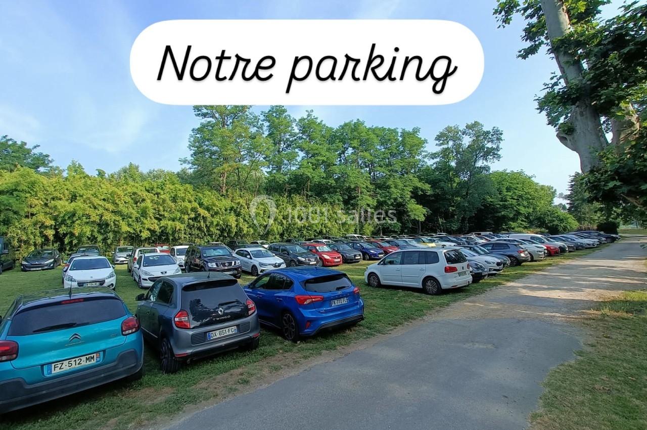 Un parking extérieur avec plusieurs voitures stationnées, entouré de verdure et d'arbres sous un ciel dégagé.