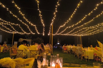 Un homme en costume soulève une femme en robe blanche dans un jardin au coucher du soleil.