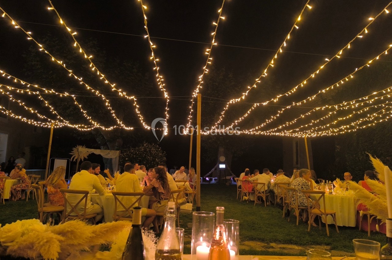 Des invités dînent en soirée sous des guirlandes lumineuses suspendues dans un jardin.