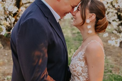 Un homme en costume soulève une femme en robe blanche dans un jardin au coucher du soleil.