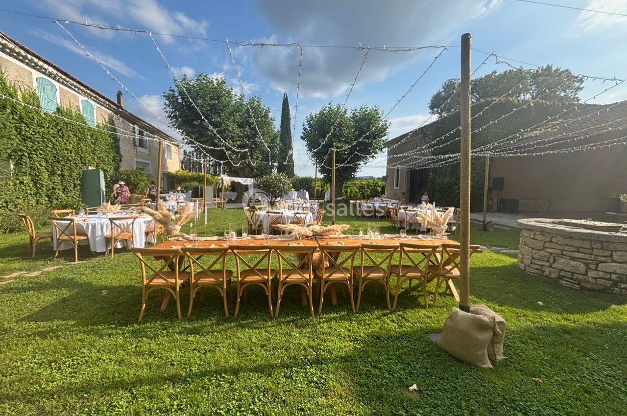 Tables et chaises en bois disposées sur une pelouse pour un événement en extérieur, entourées de bâtiments et de guirlandes…