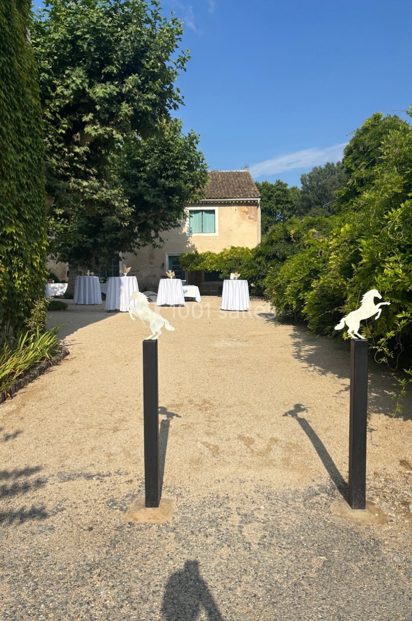 Allée gravillonnée bordée de verdure menant à une maison avec des tables dressées en arrière-plan.