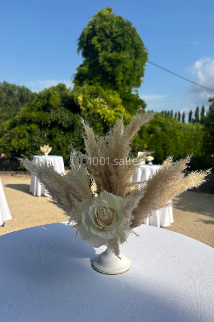 Centre de table avec une rose blanche et des herbes de la pampa, posé sur une nappe blanche en extérieur.