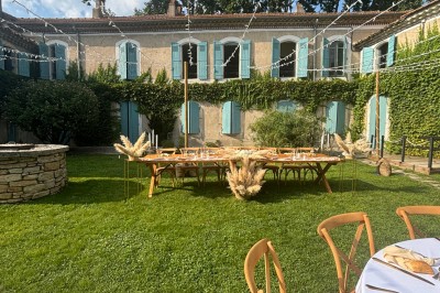 Table en bois à l'extérieur avec des plantes en pot, une boîte aux lettres verte, des paniers et un photomaton en arrière…