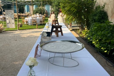 Table en bois à l'extérieur avec des plantes en pot, une boîte aux lettres verte, des paniers et un photomaton en arrière…