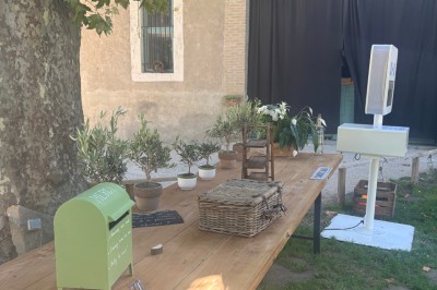 Table en bois à l'extérieur avec des plantes en pot, une boîte aux lettres verte, des paniers et un photomaton en arrière…