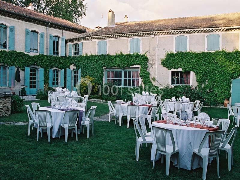 Tables dressées avec nappes blanches et chaises en plastique dans la cour d'une maison ancienne couverte de lierre.