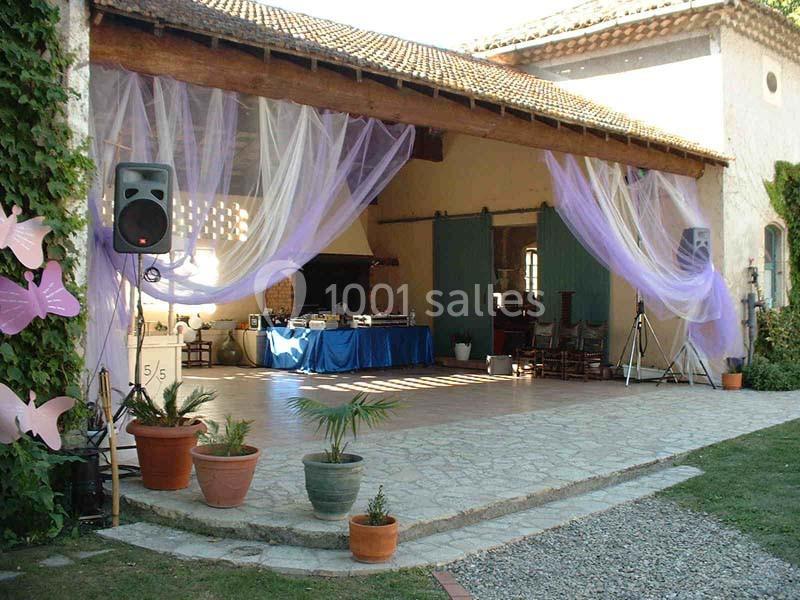 Espace extérieur couvert décoré de voilages violets, avec tables, chaises et matériel audio sur une terrasse pavée.