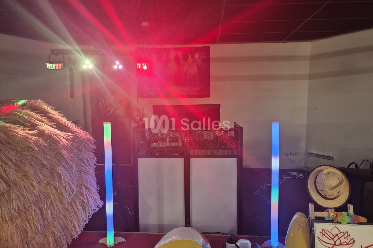 Installation de DJ éclairée en rouge, avec barres lumineuses LED bleues et vertes, projecteurs au plafond et décor de type paille sur la gauche.