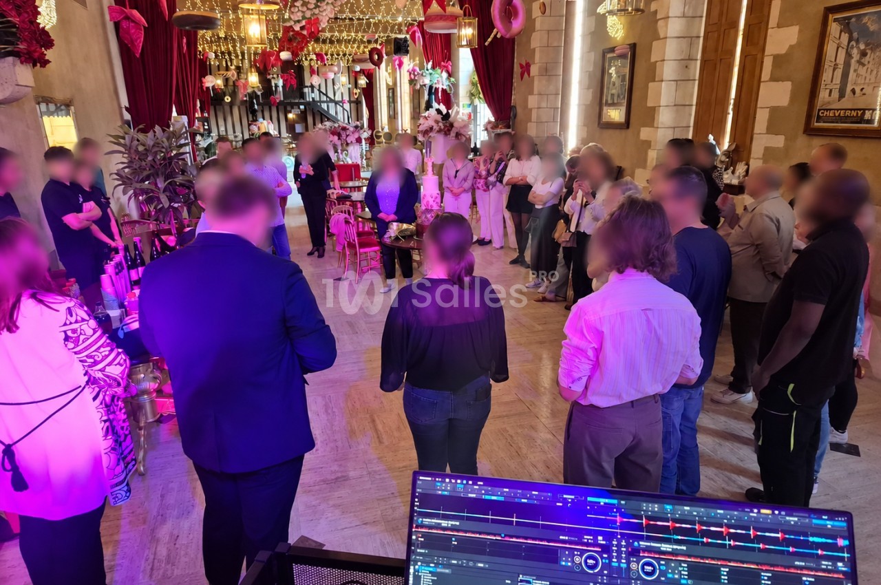 Invités debout en demi-cercle dans une salle aux rideaux rouges, face à un gâteau, pupitre de mixage au premier plan.