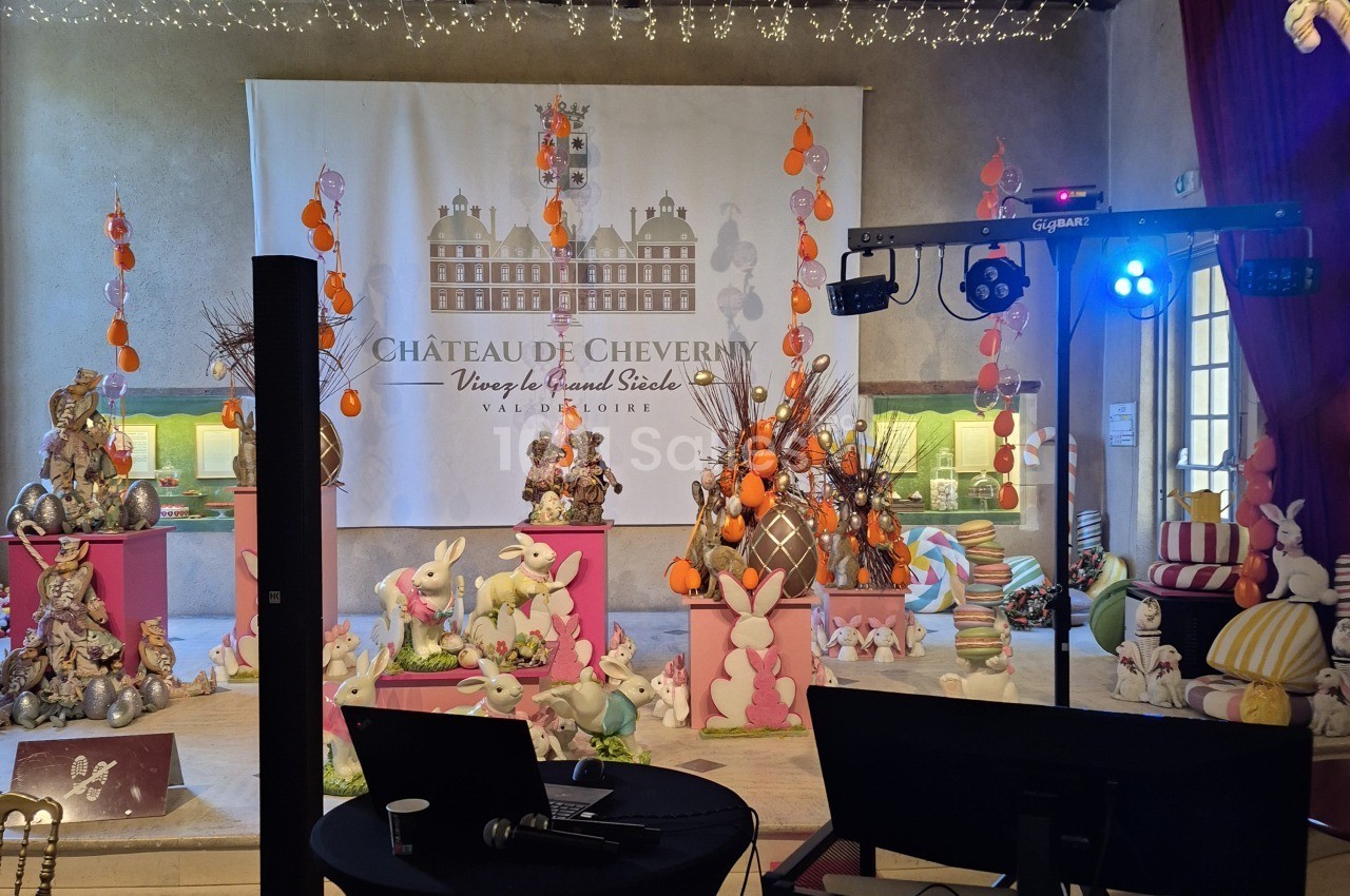Salle décorée pour Pâques de lapins et d'œufs décoratifs, avec un poste DJ au premier plan, ordinateur et micro.