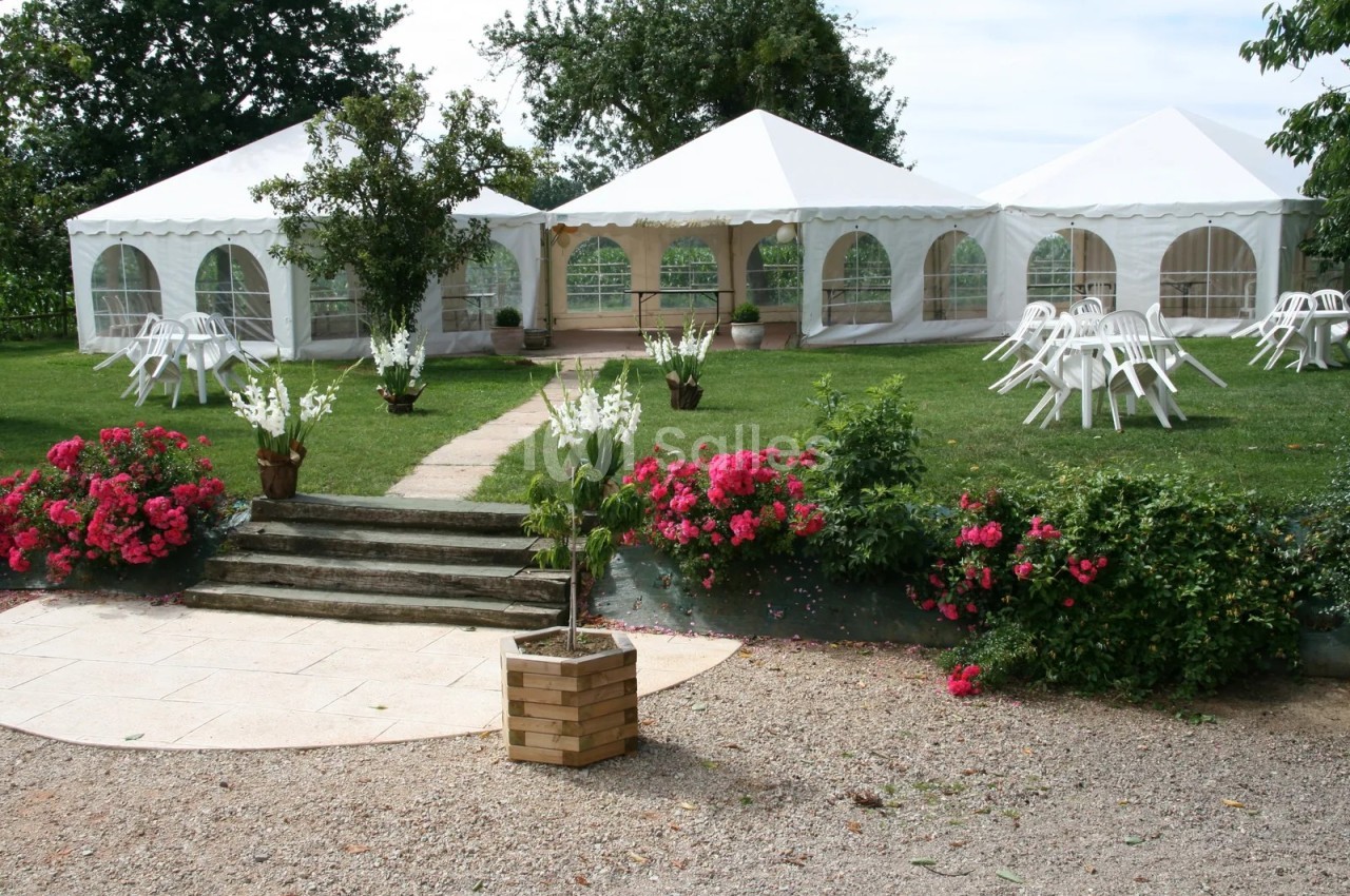 Jardin verdoyant avec trois grands chapiteaux blancs à fenêtres arrondies, tables et chaises en plastique blanc disposées sur la pelouse, massifs de fleurs roses. Count characters: roughly 160? Let's count: "Jardin verdoyant avec trois grands chapiteaux