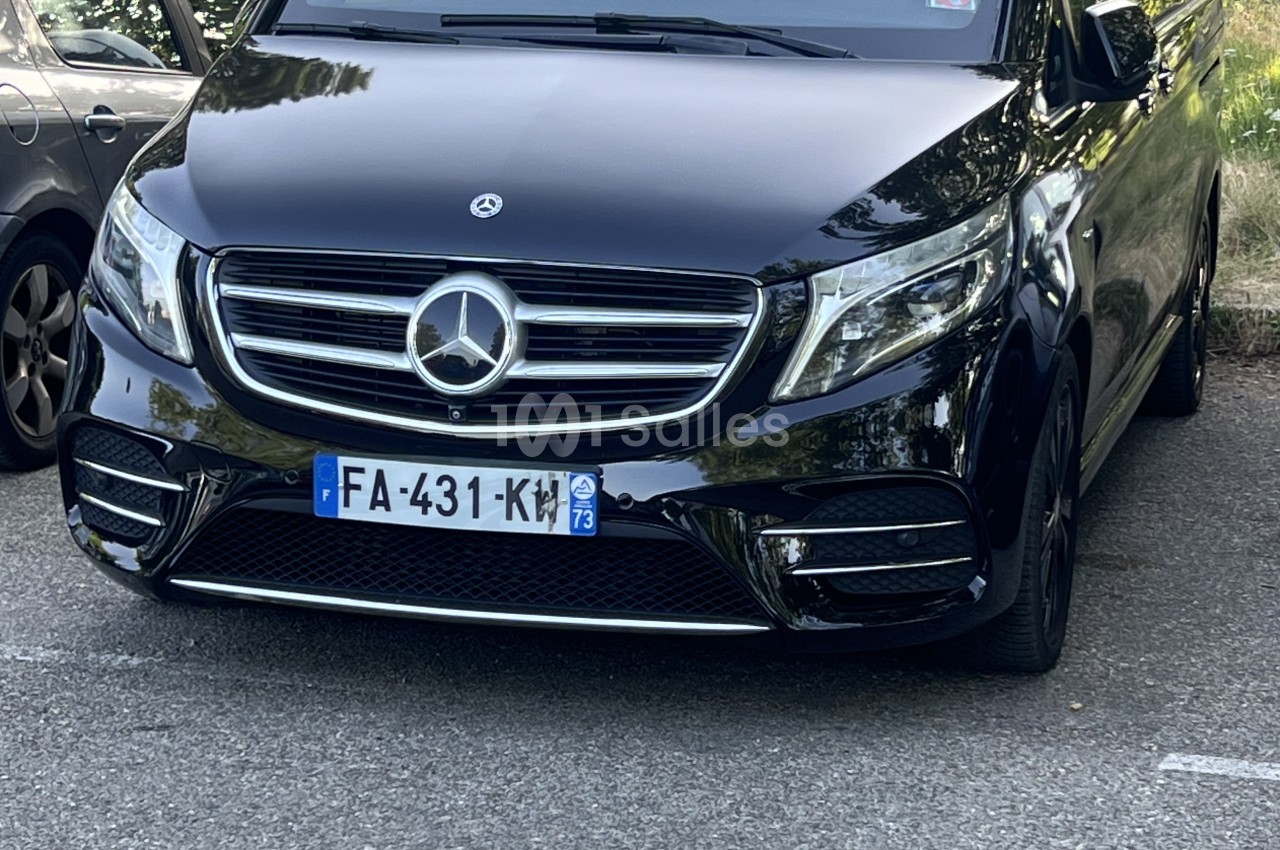 Monospace Mercedes-Benz noir vu de face, garé en extérieur sur un parking à côté d'une voiture grise.